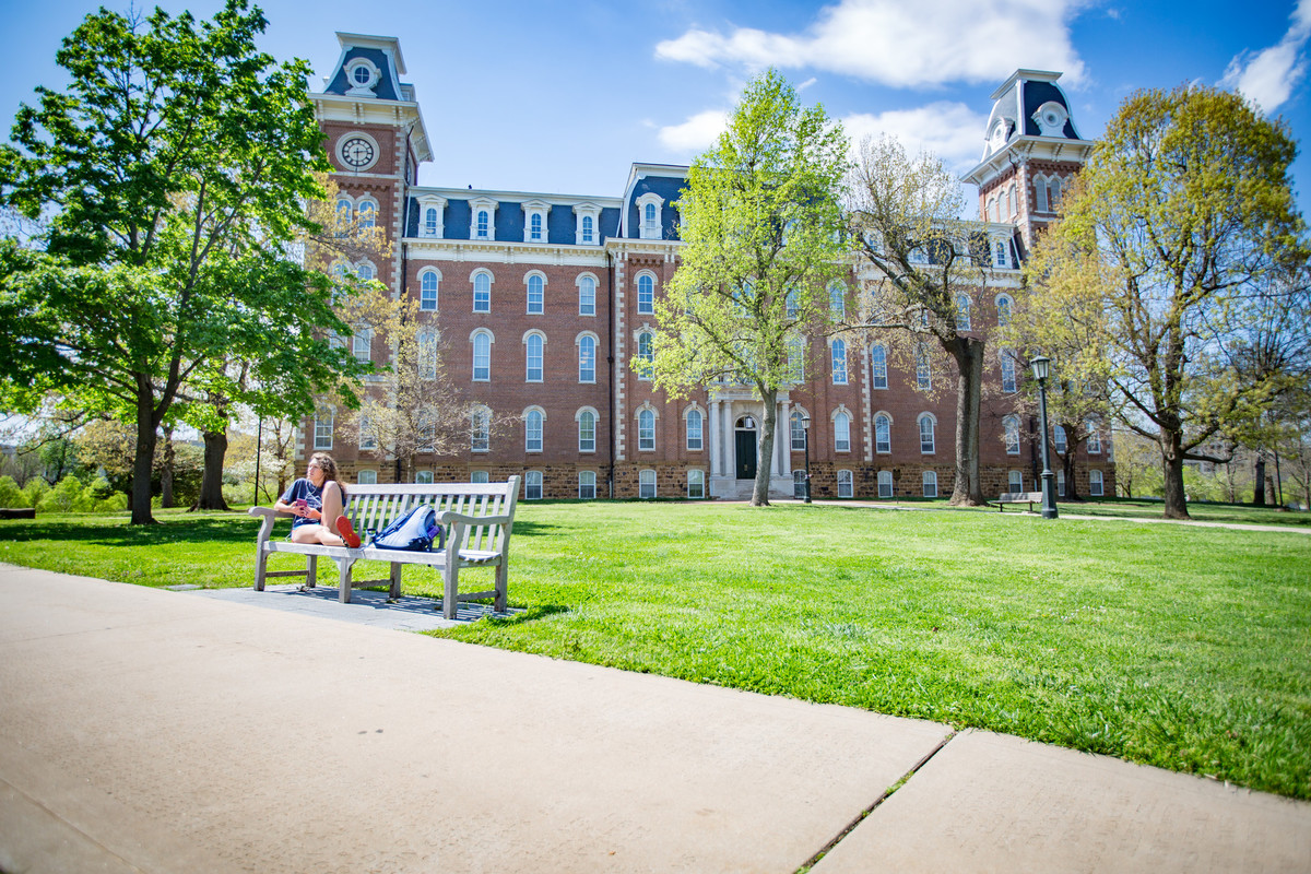 Old Main in the sumer, students sit on the bench