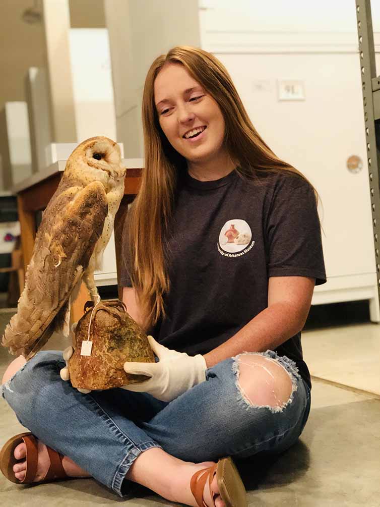 Museum Intern sitting in the collections holding an owl specimen.